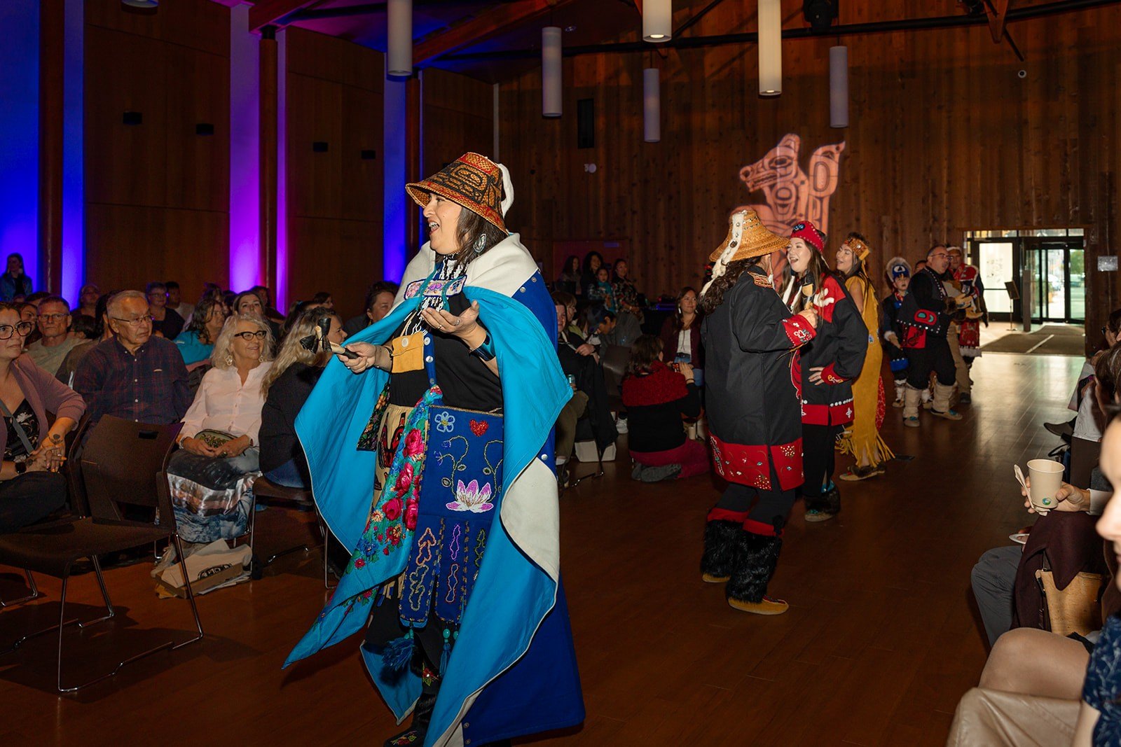 Dakhká Khwáan Dancers in regalia perform in the hall as seated guests watch.